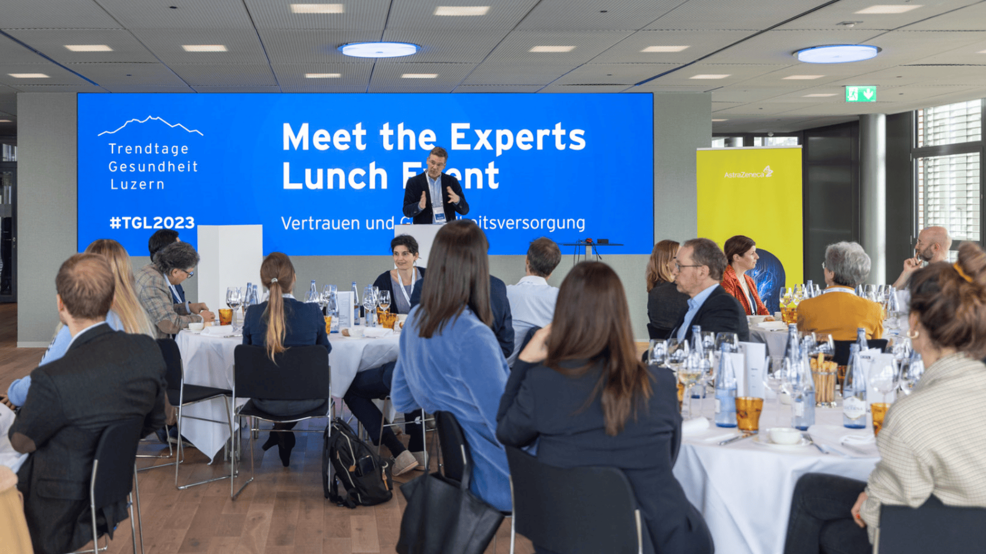 Ein Referent stellt sich am Meet the Experts Lunch Event der Trendtage Gesundheit Luzern 2023 dem an runden Tischen sitzenden Publikum vor. Die Veranstaltung findet in einem modernen, hellen Konferenzraum statt.