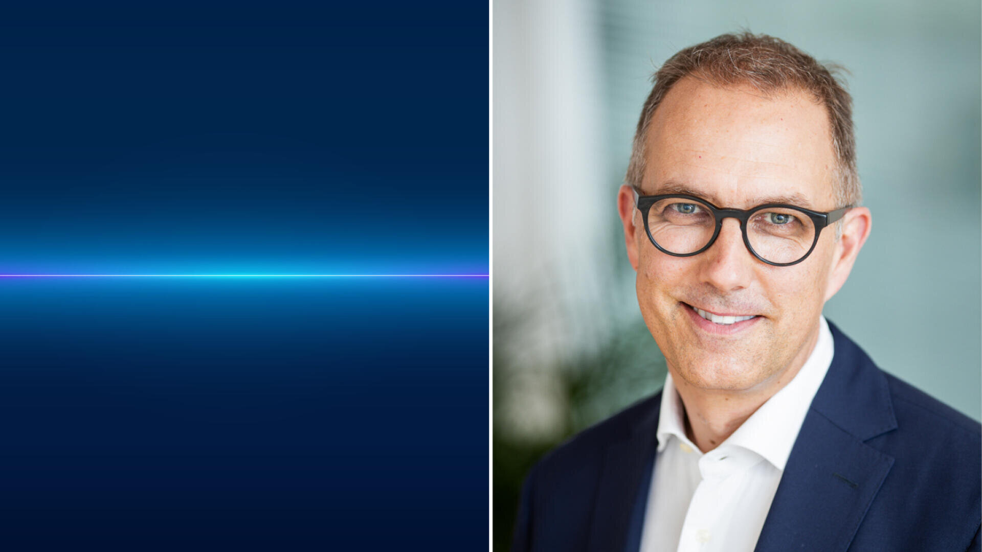 Ein Mann in einem Anzug und mit Brille lächelt in die Kamera. Er hat kurzes hellbraunes Haar und steht vor einem unscharfen Hintergrund. Das Bild ist geteilt; die linke Seite zeigt einen blauen Farbverlauf mit einer horizontalen leuchtenden Linie.